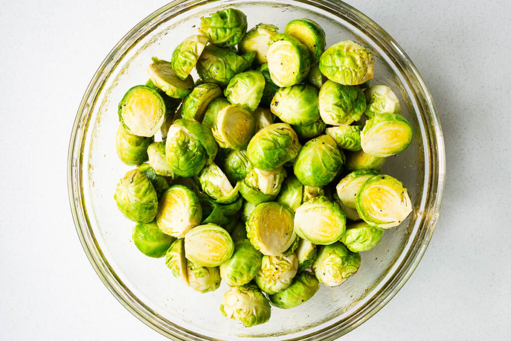 Halved Brussels sprouts coated in honey sauce in a large glass mixing bowl.