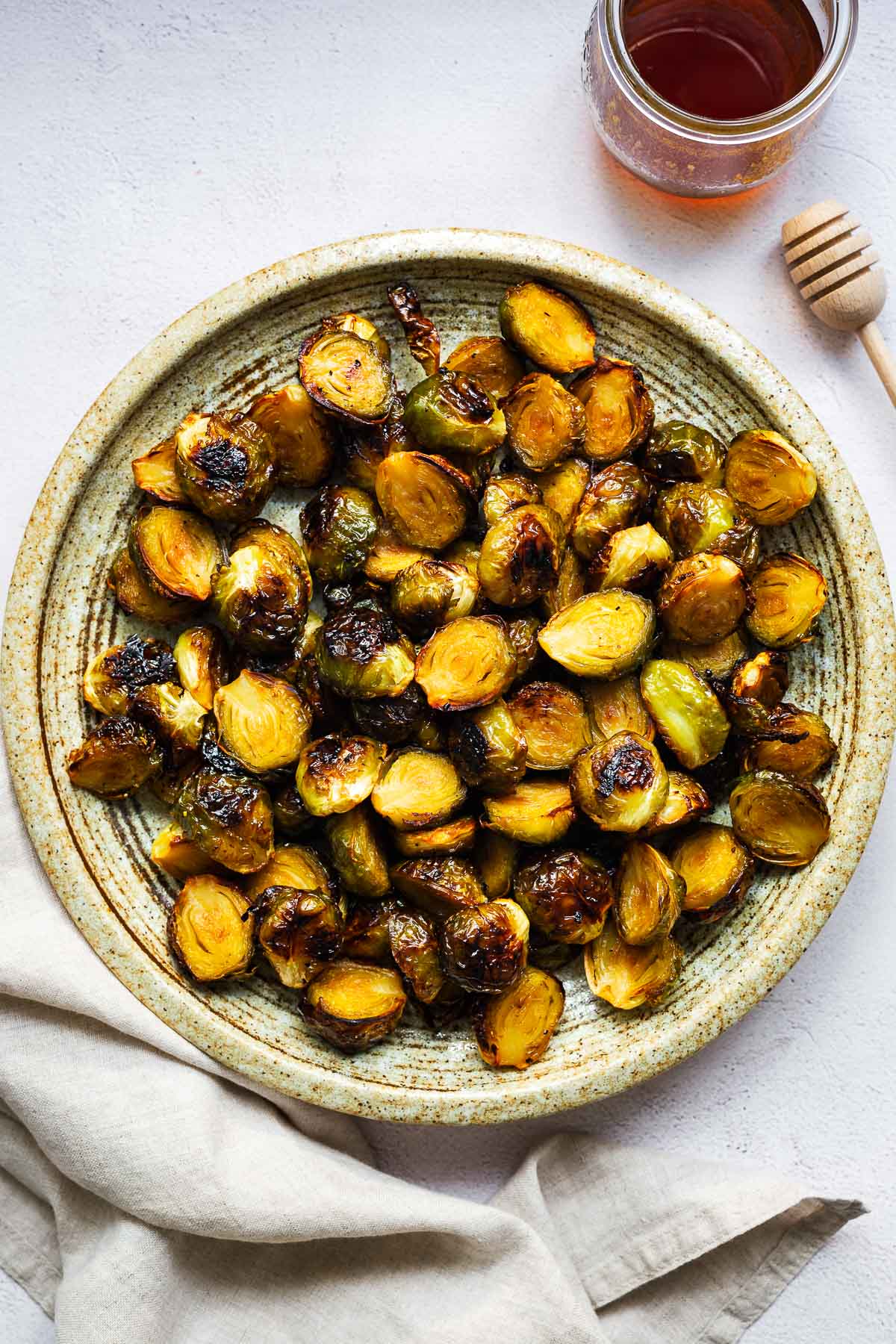 Hot honey roasted Brussels sprouts on a ceramic serving plate viewed from above next to a jar of hot honey.