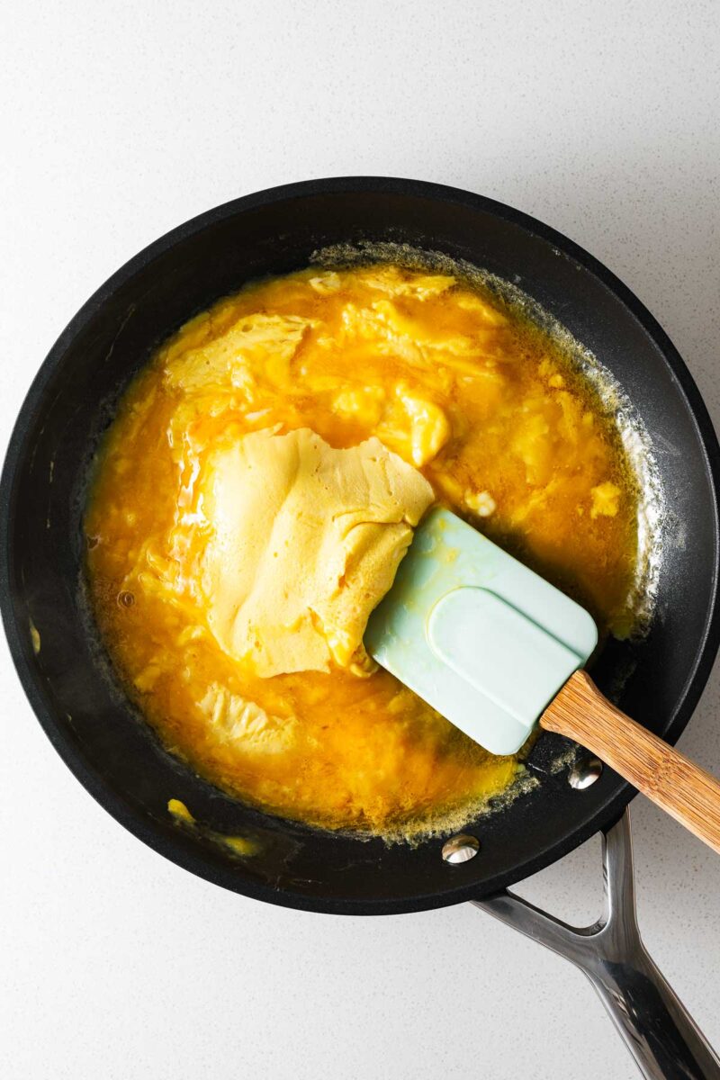Scrambling whisked miso eggs in a nonstick pan using a gentle flipping technique as viewed from above.