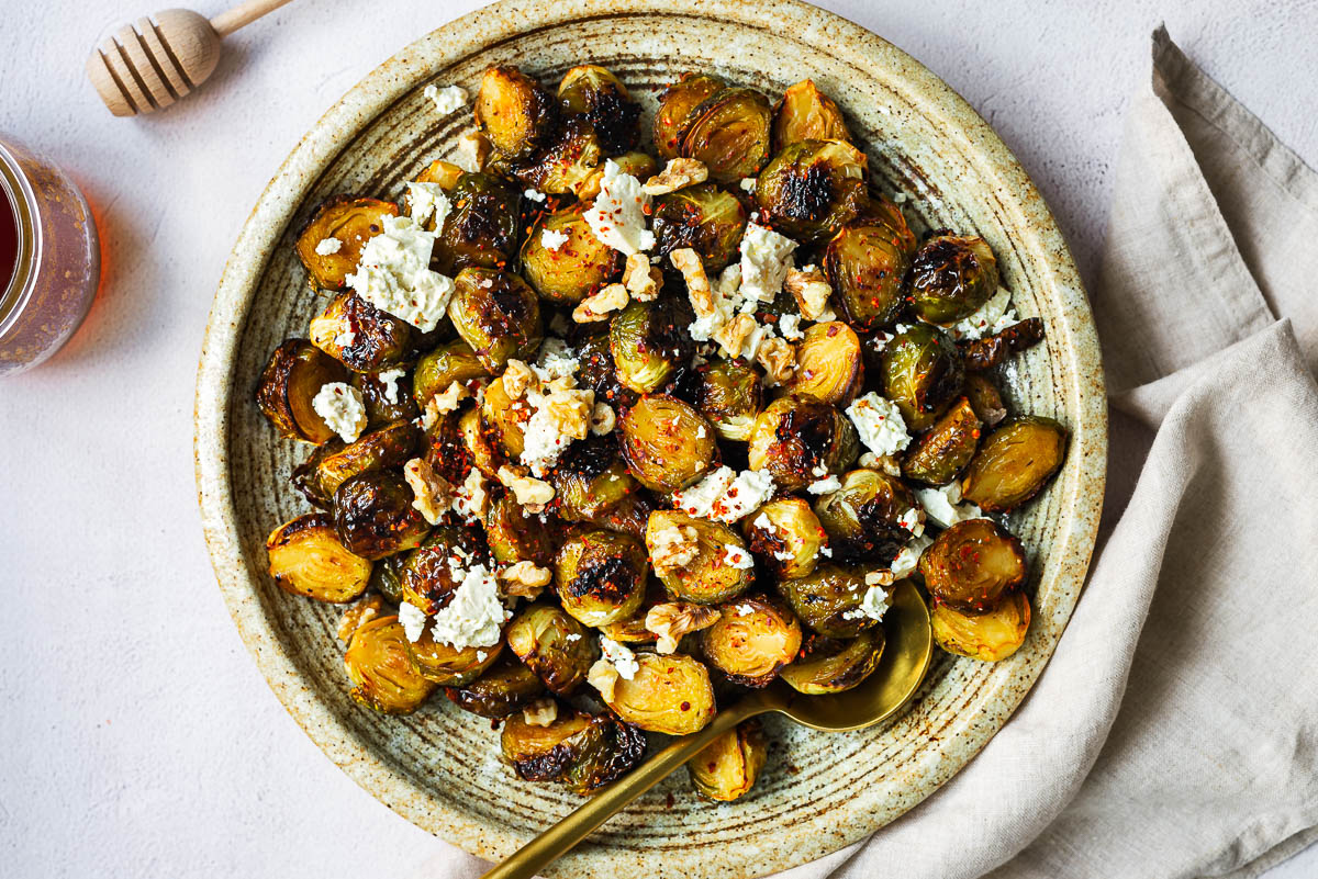 Roasted Brussels sprouts with honey glaze topped with feta and walnuts in a shallow serving bowl.