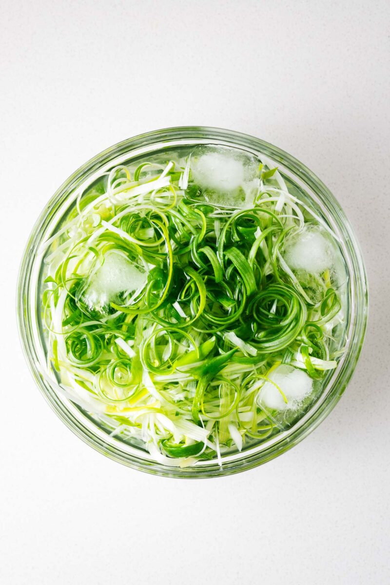 Sliced scallions (green onions) in a glass bowl filled with ice and water.