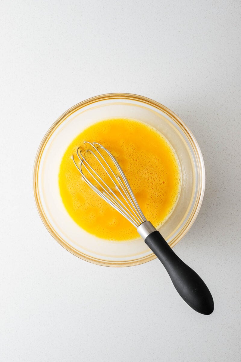 Whisked eggs with sugar in a glass bowl with a balloon whisk.