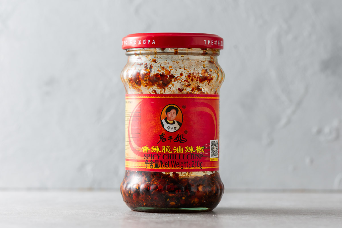 An almost empty jar of Chinese chilli crisp against a grey background.