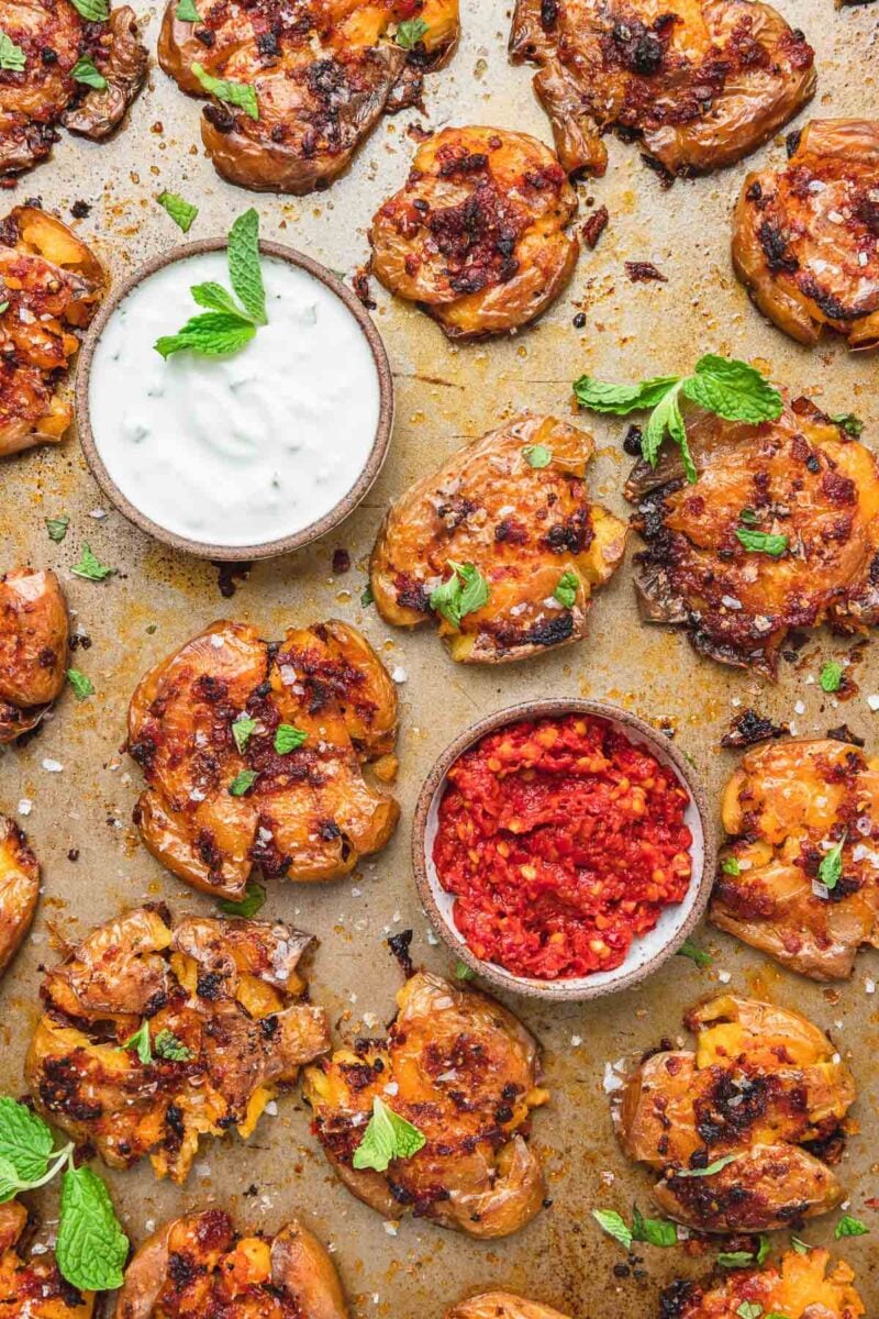 Squashed roasted harissa potatoes on a sheet pan viewed from above.