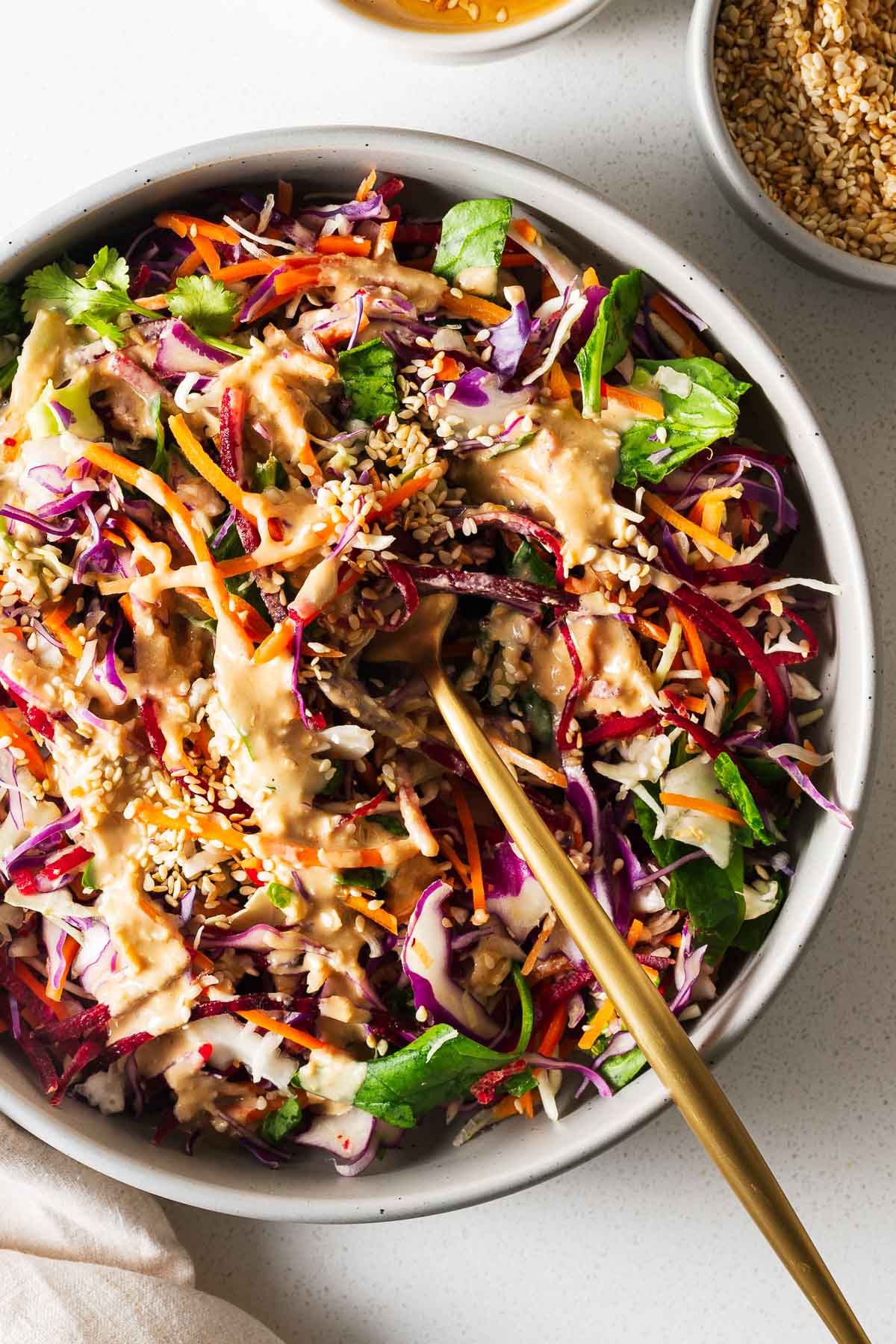 A close-up of shredded rainbow slaw drizzled with tahini miso dressing and sprinkled with sesame seeds.