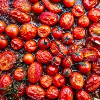 Top down view of a baking sheet with roasted cherry tomatoes in a harissa marinade.
