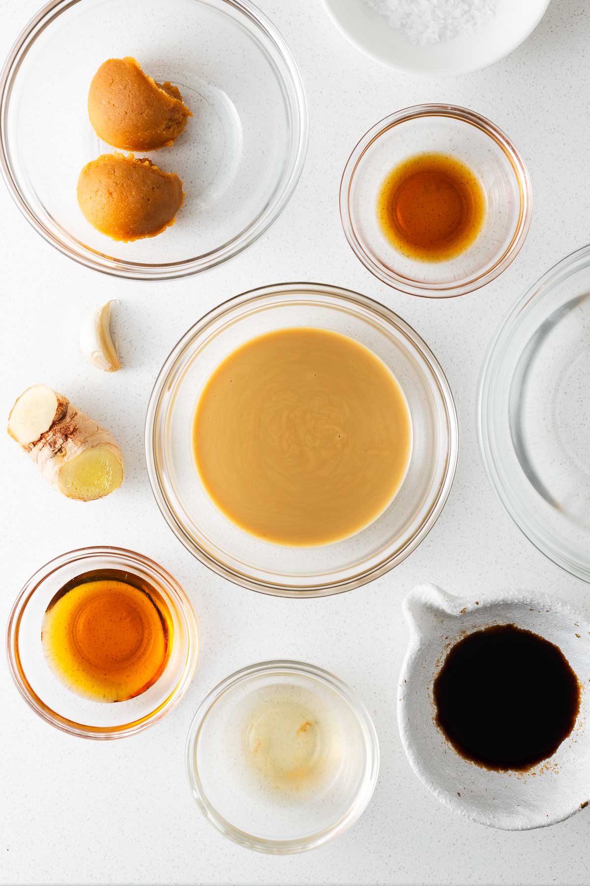 The ingredients for tahini miso dressing arranged in small glass bowls viewed from above.