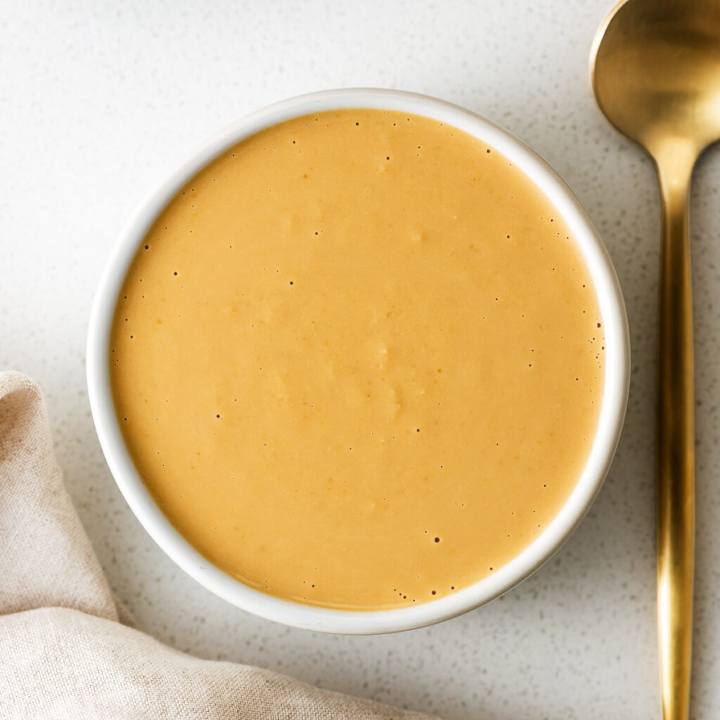 Tahini miso dressing in a small white bowl next to a golden teaspoon.