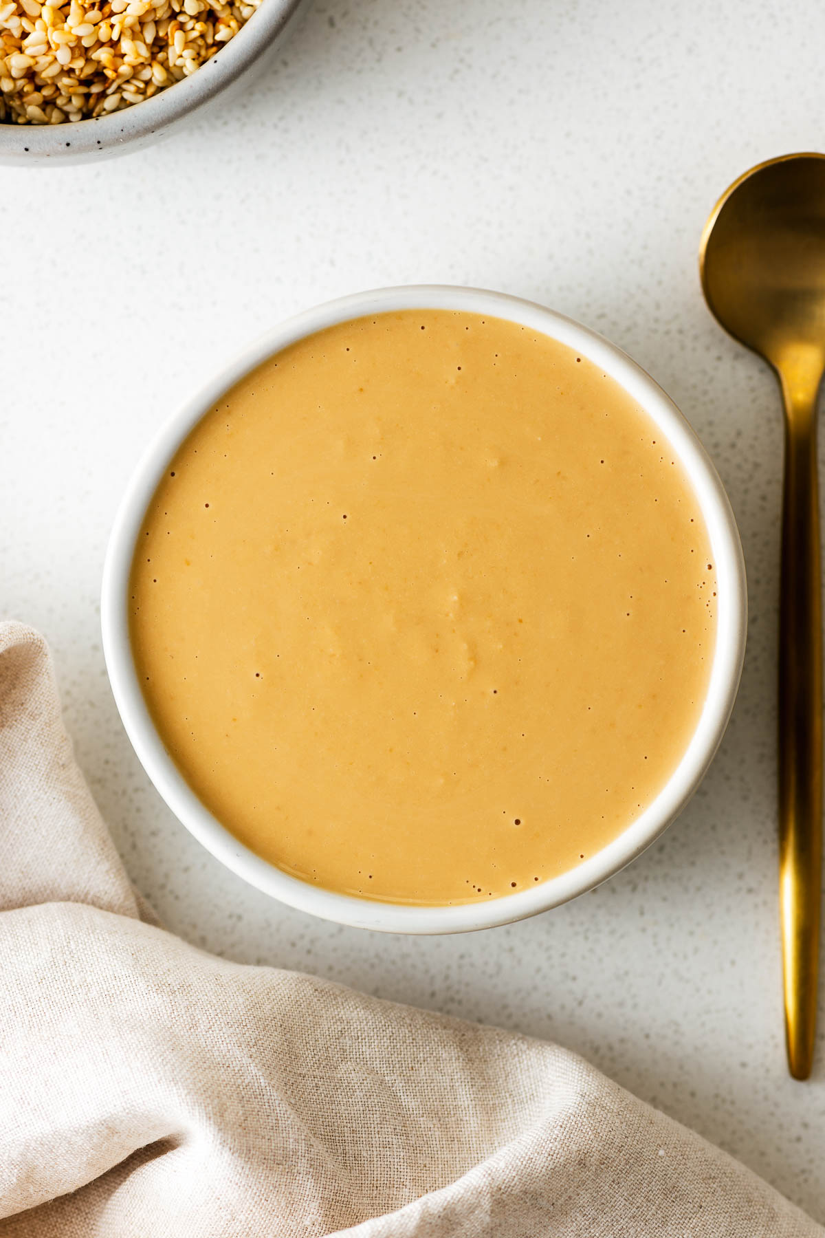 Tahini miso dressing in a small white bowl next to a golden teaspoon.