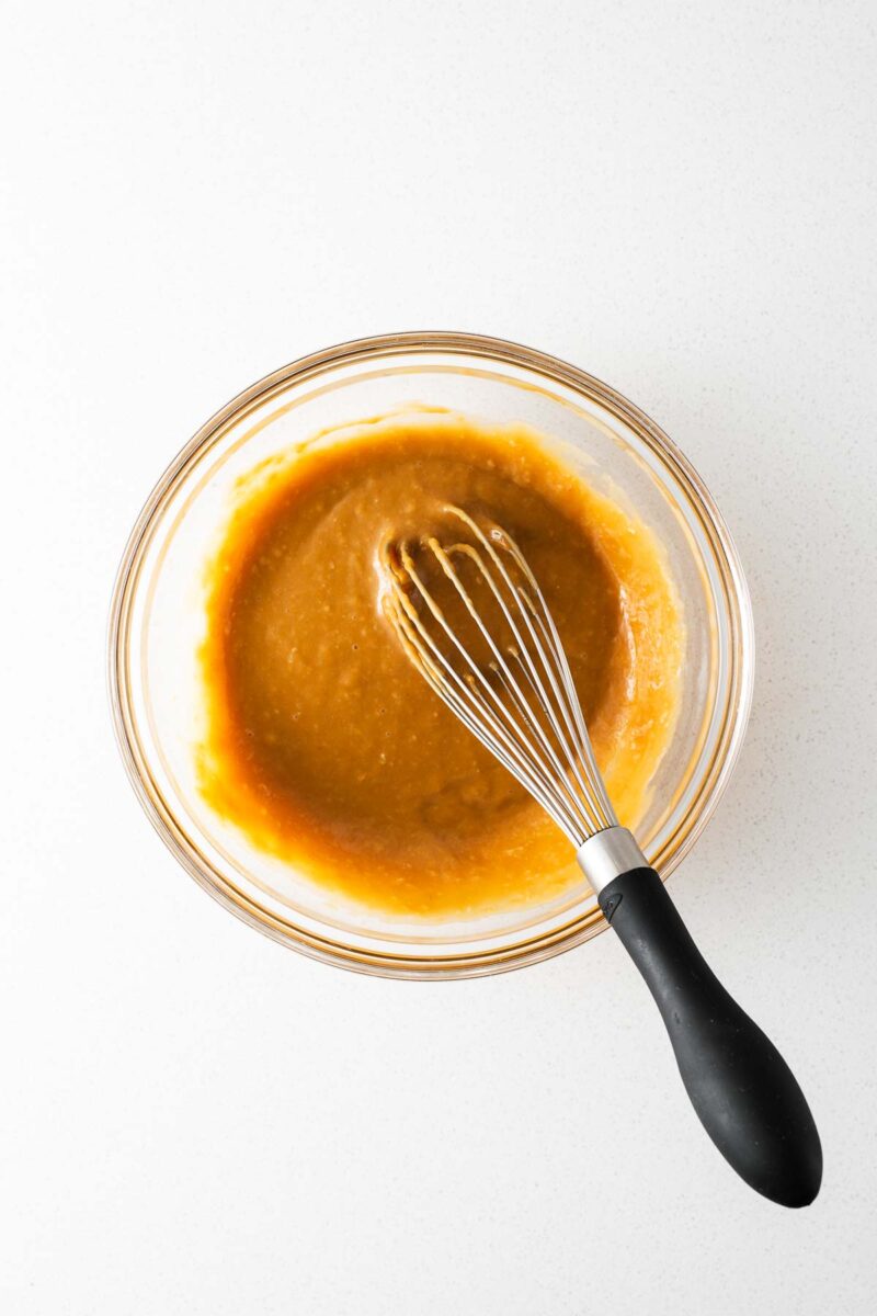 Salad dressing with miso, ginger and tahini in a glass bowl with a whisk.