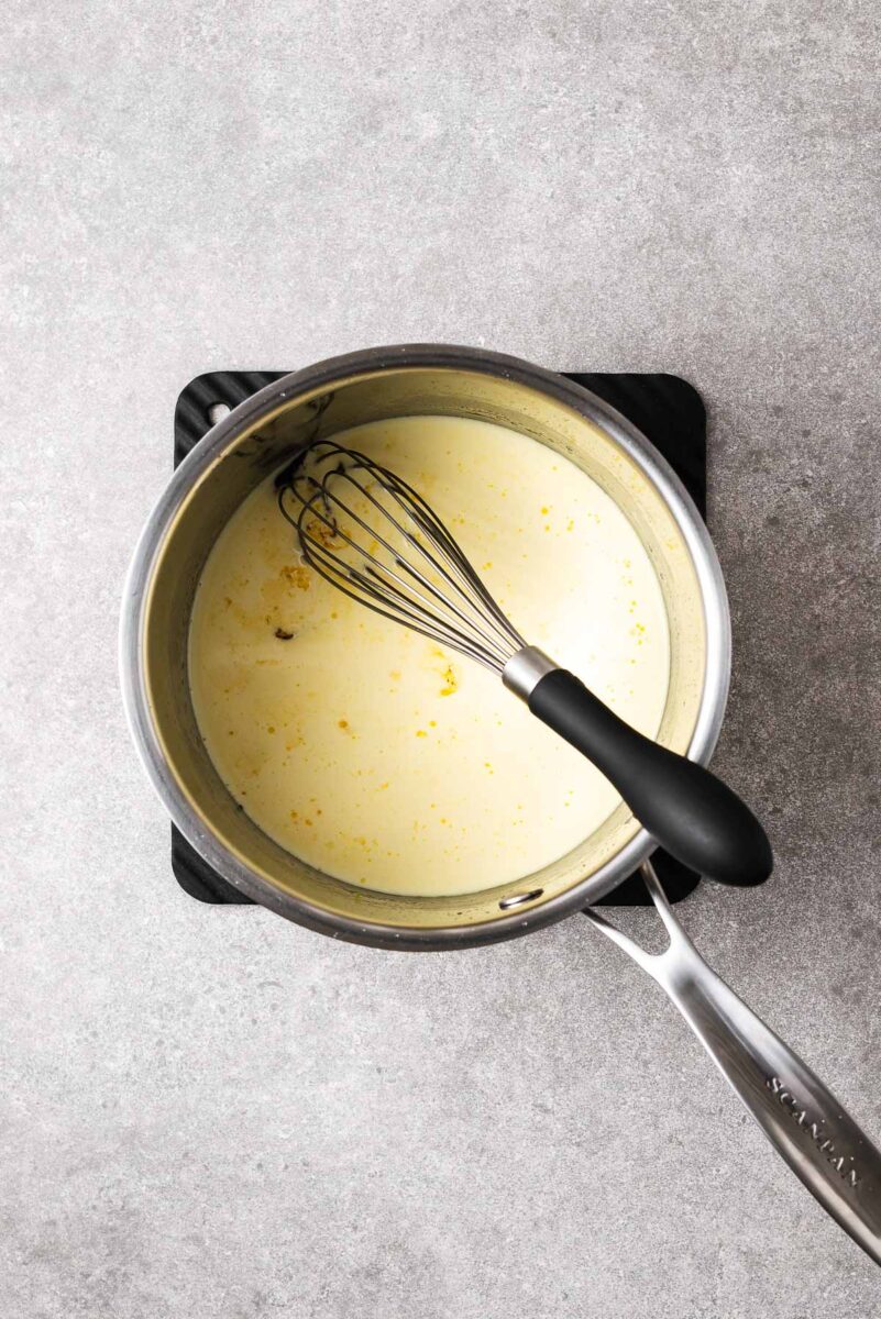 A stainless steel saucepan with cream poured over sugar syrup before getting whisked together.