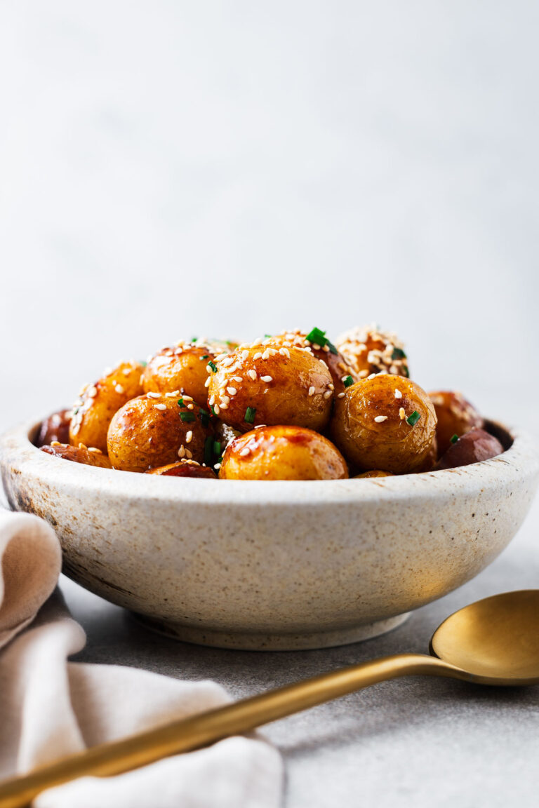 A bowl with gamja jorim (Korean braised potatoes) viewed from the side next to a gold serving spoon.