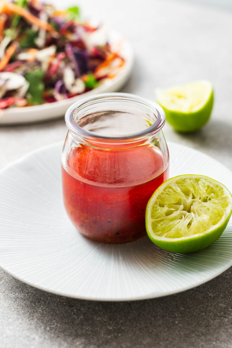 A glass jar of chilli lime dressing with a squeezed lime.