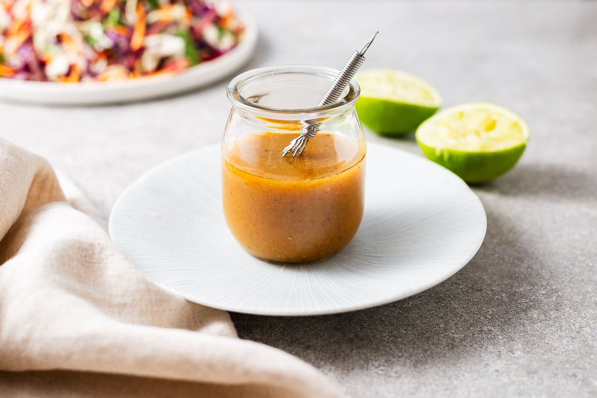 Homemade miso and lime vinaigrette in a glass jar with a salad in the background next to spent fresh limes.