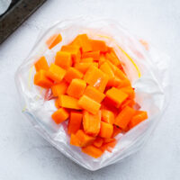 A resealable plastic bag with frozen blanched carrots in a large dice.
