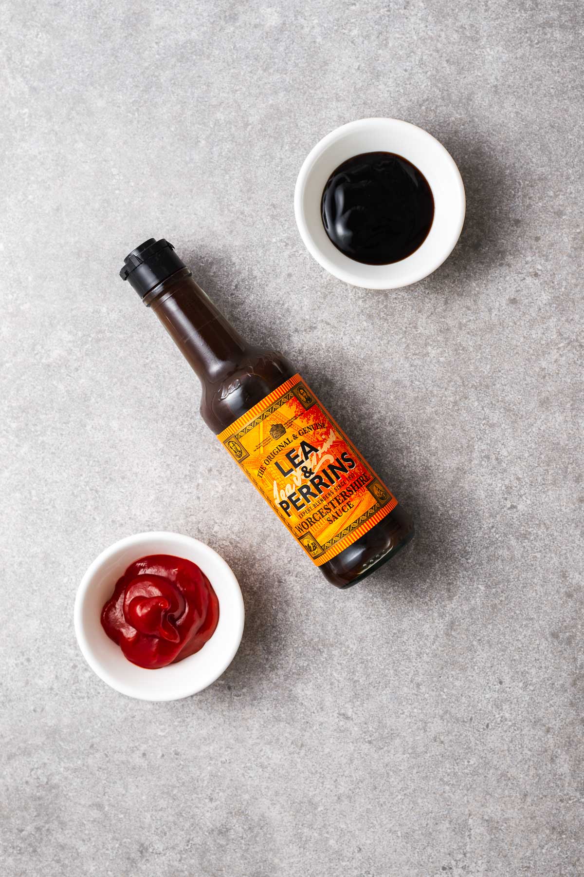 A bottle of Lea & Perrins Worcestershire sauce with two small bowls holding tomato ketchup and sweet soy sauce.