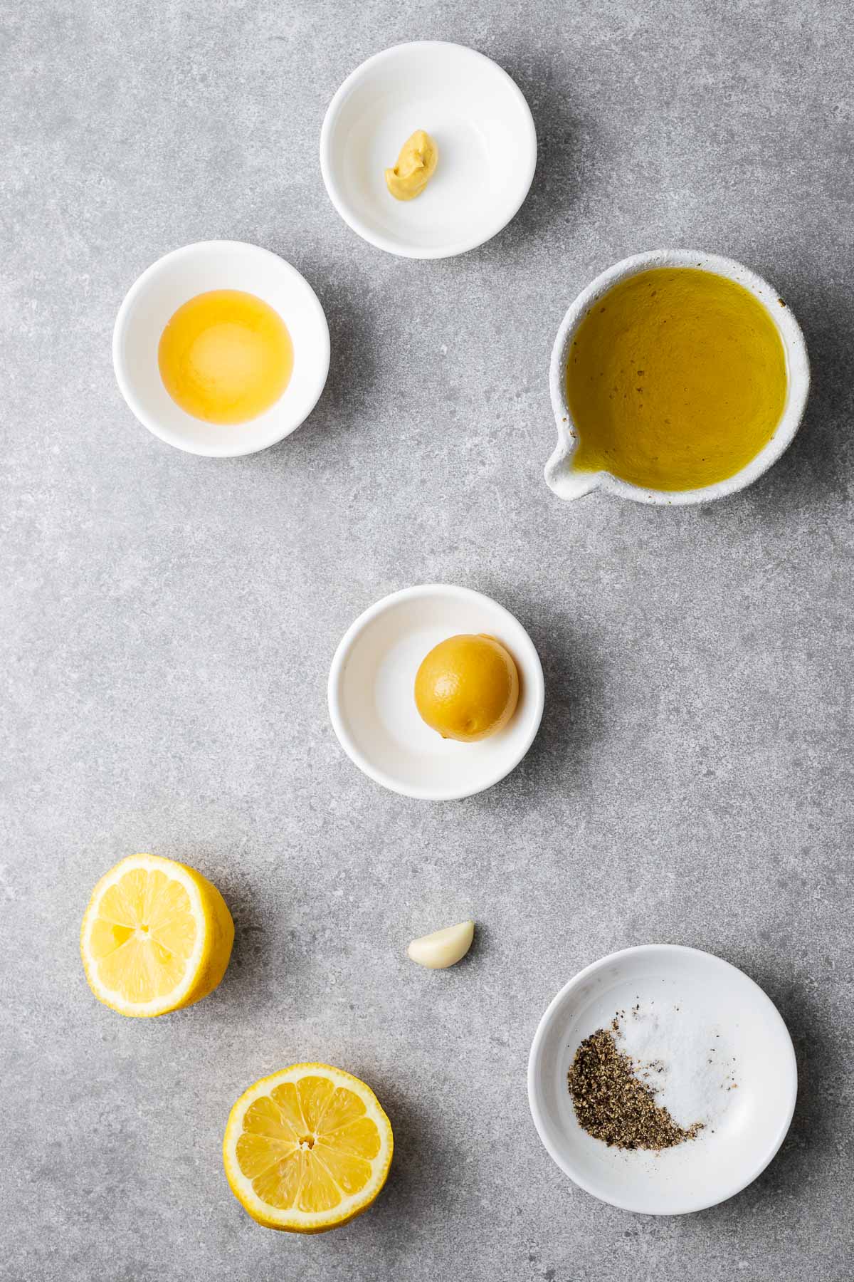 Ingredients for preserved lemon vinaigrette including fresh lemons, preserved lemon, a garlic clove, honey, Dijon mustard, and extra virgin olive oil with salt and pepper.