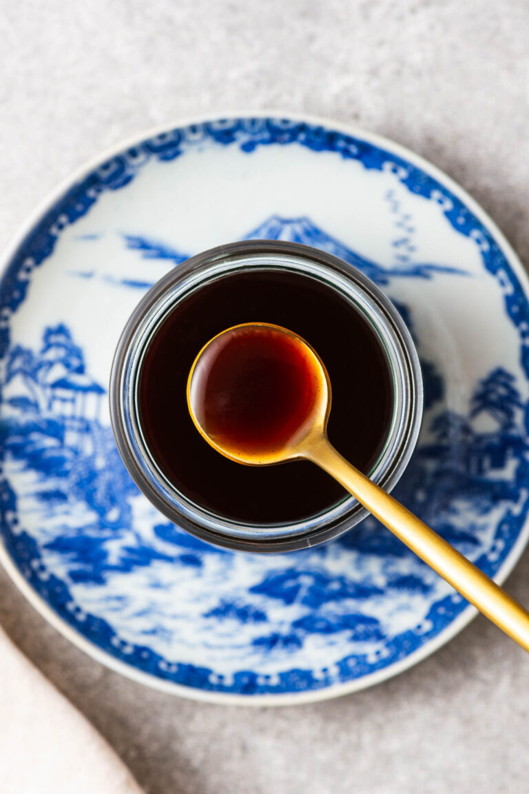 A spoon of yakisoba sauce from a glass jar placed on Japanese crockery.