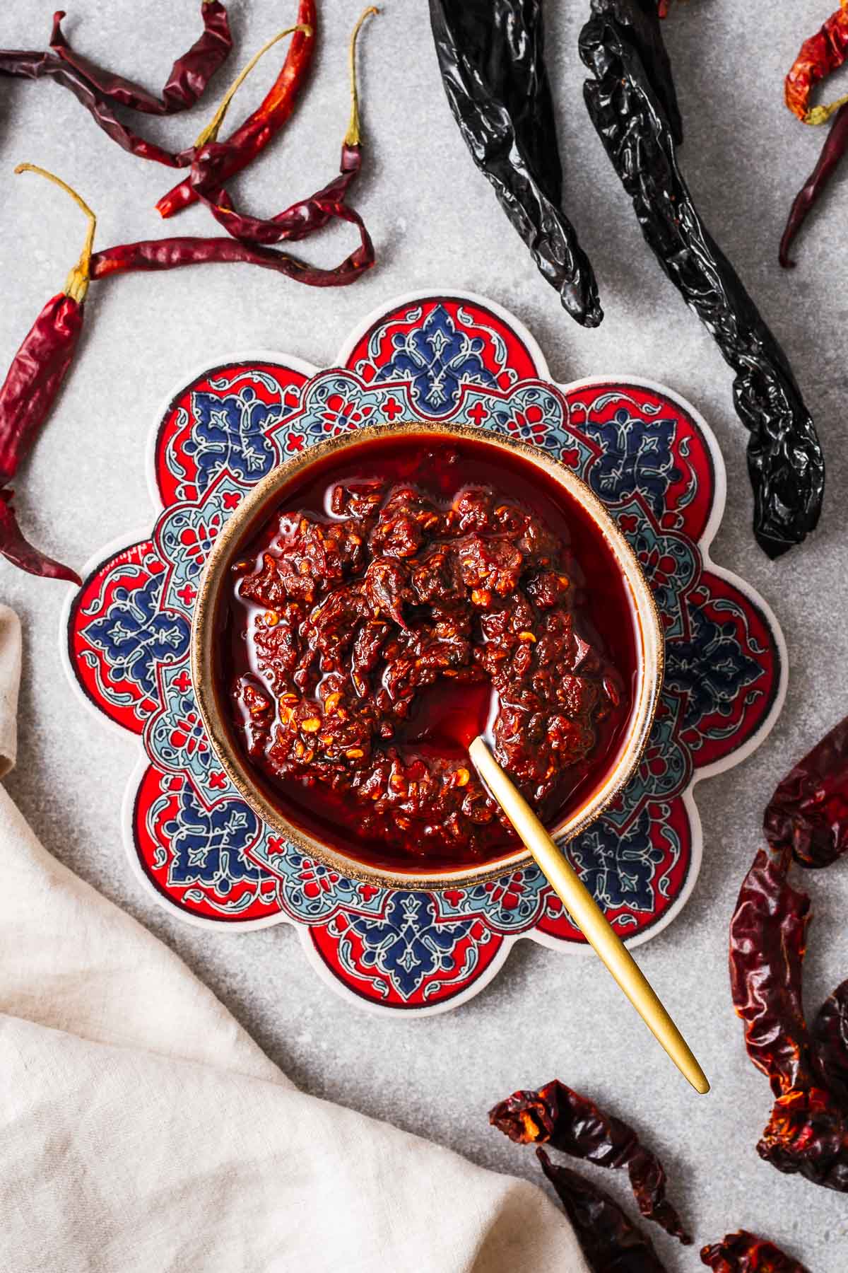 Homemade harissa paste in a small bowl surrounded by different types of dried chile peppers.