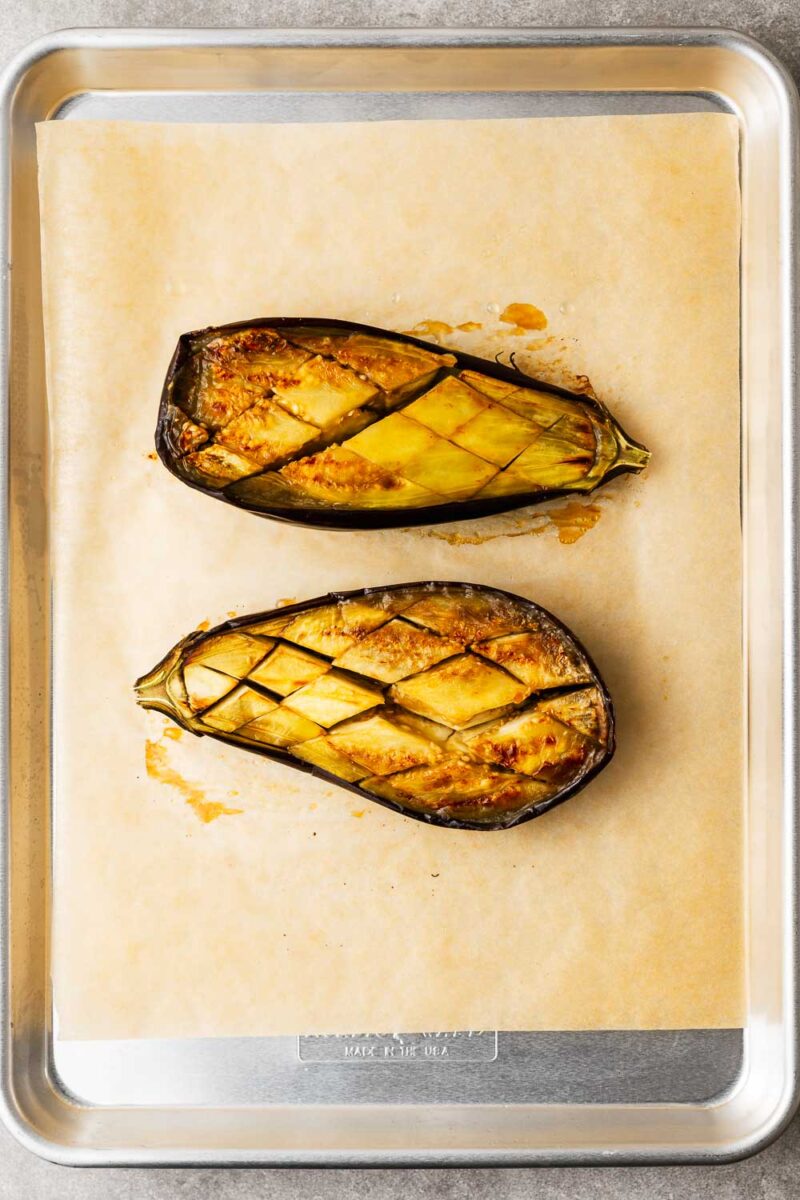 Oven-baked aubergine halves, cut-side up, on a parchment-lined baking sheet.