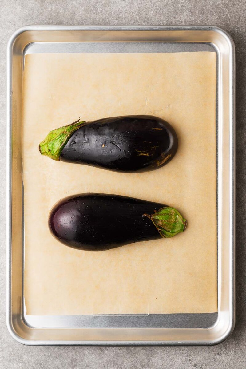Oiled eggplant placed cut-side down on a parchment-lined baking sheet.