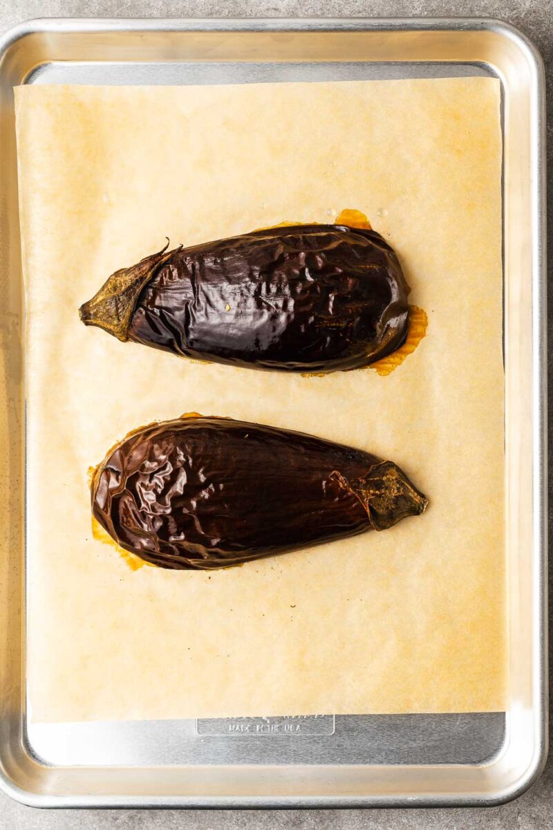 Oven-baked eggplant halves, skin-side up, on a parchment-lined baking sheet.