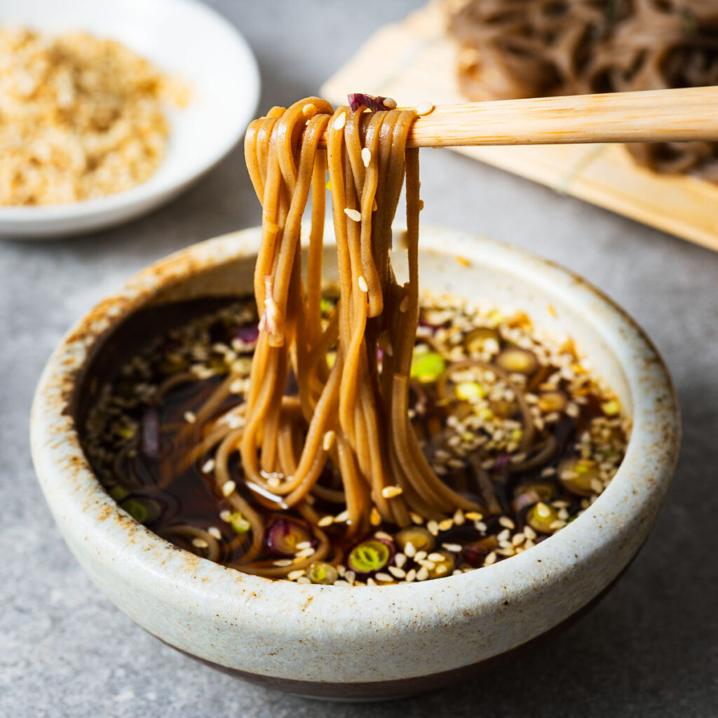Soba noodles dipped into Japanese mentsuyu dipping sauce with chopsticks.