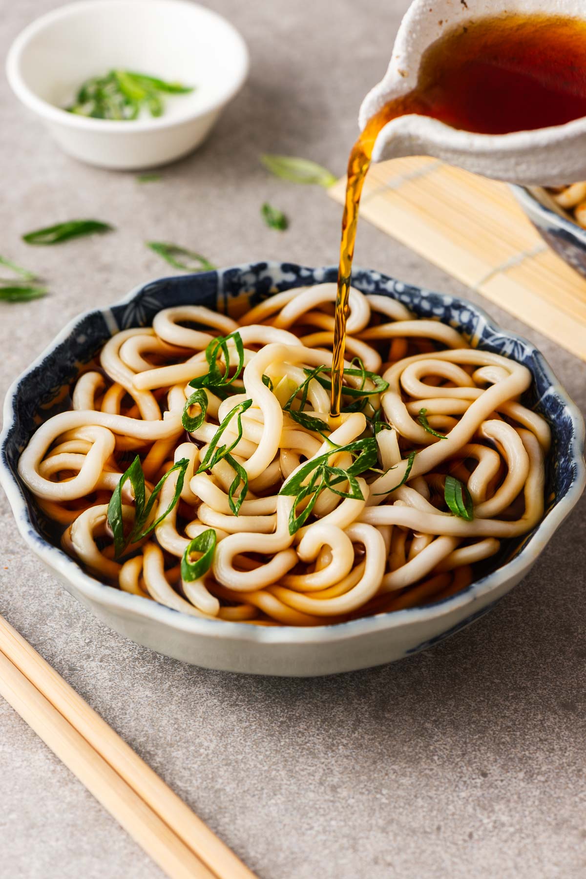 Pouring kake udon noodle broth over a Japanese bowl with udon noodles.