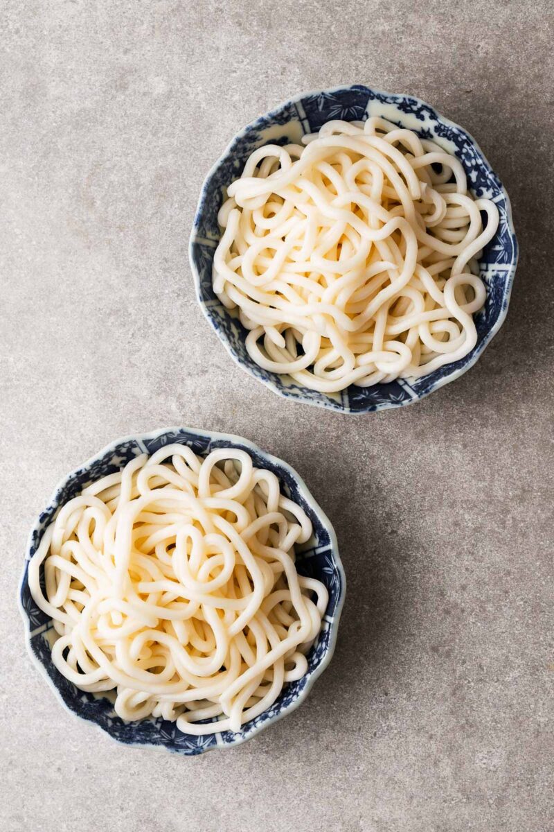 Two bowls with cooked udon noodles.