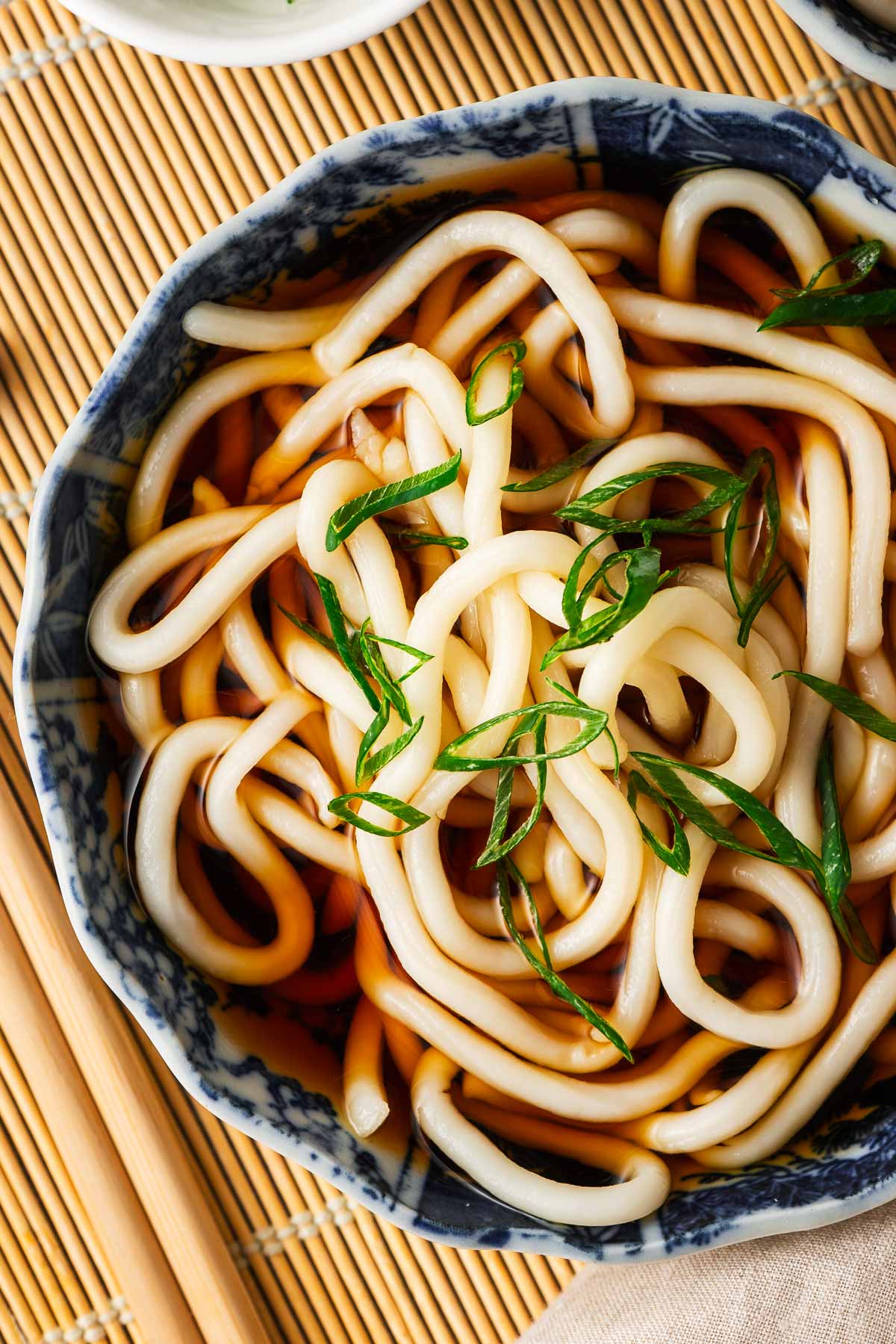 Thick and chewy udon noodles in a bowl of udon broth scattered with sliced green onions.