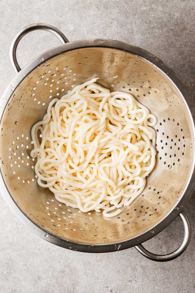 A colander with rinsed and drained udon noodles looking plump and chewy.
