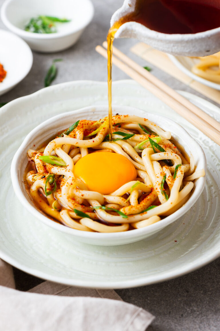 Pouring broth over udon noodles with a raw egg yolk for tsukimi udon.