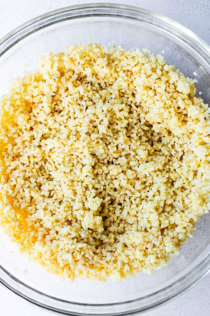 Cooked bulgur wheat in a large glass mixing bowl.