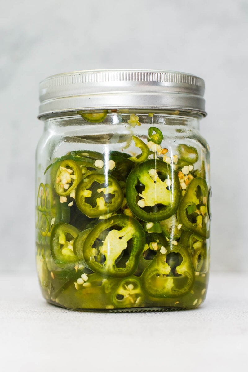 Fermented chillies in a mason jar showing the salty fermentation liquid pooling at the bottom of the jar.
