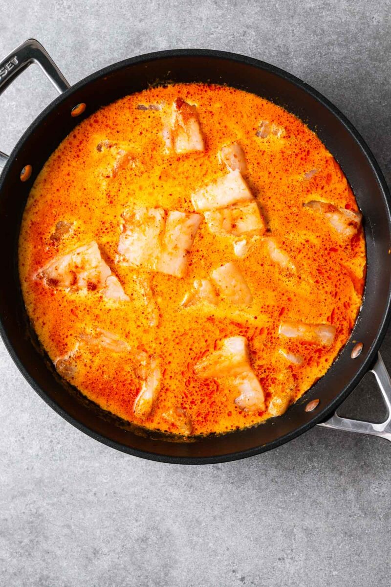 Large even-sized chunks of raw white fish fillets in a red curry coconut sauce.