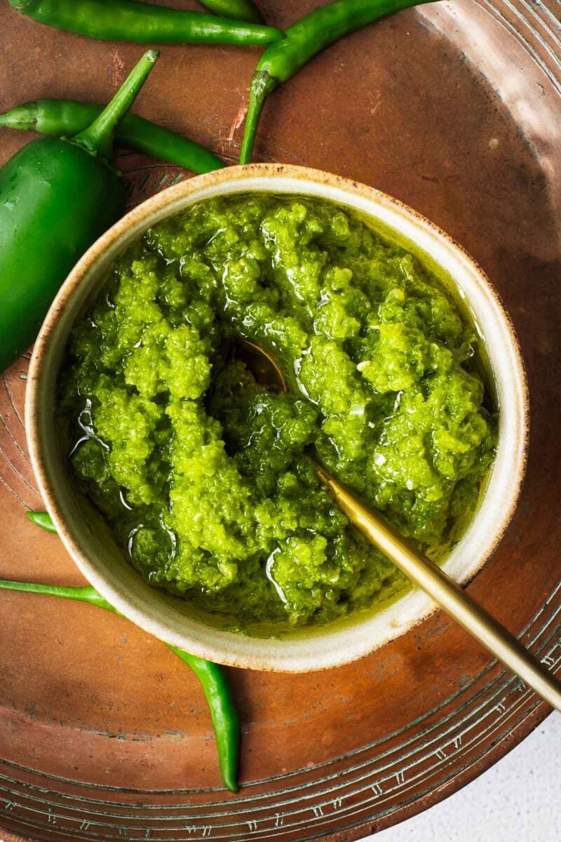 A bowl with chunky green shatta topped with olive oil.