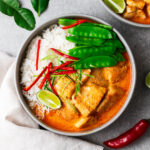 A bowl with steamed jasmine rice, Thai fish red curry and snow peas topped with sliced red chile and kaffir lime leaves.