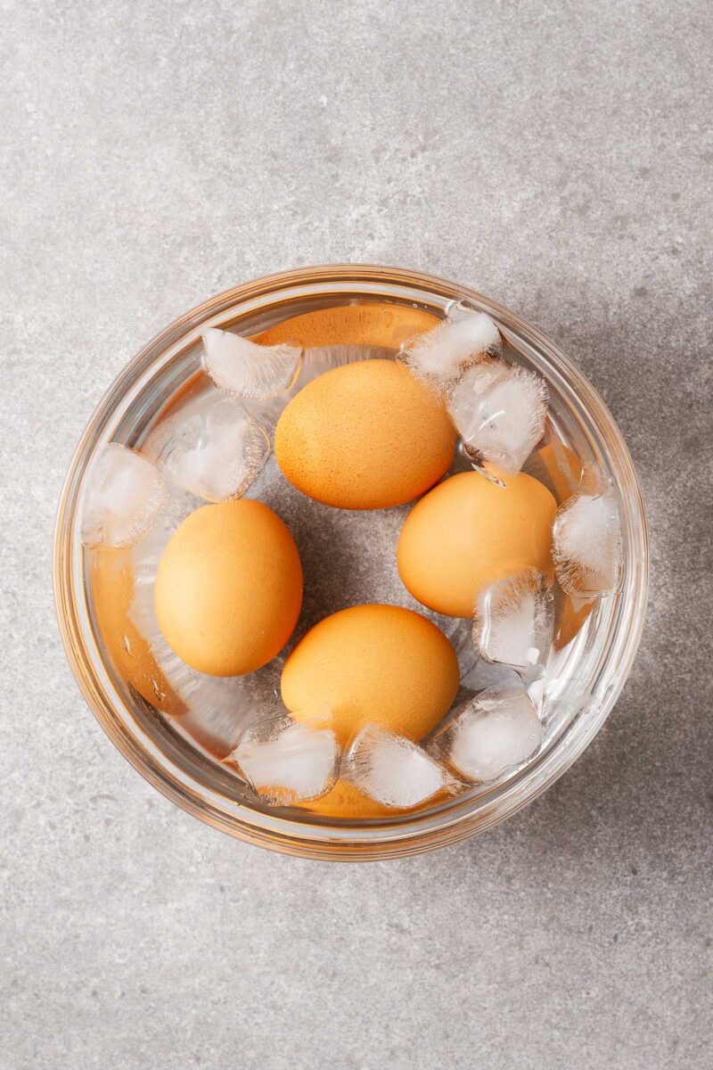 Four boiled eggs in a bowl of water with ice cubes.