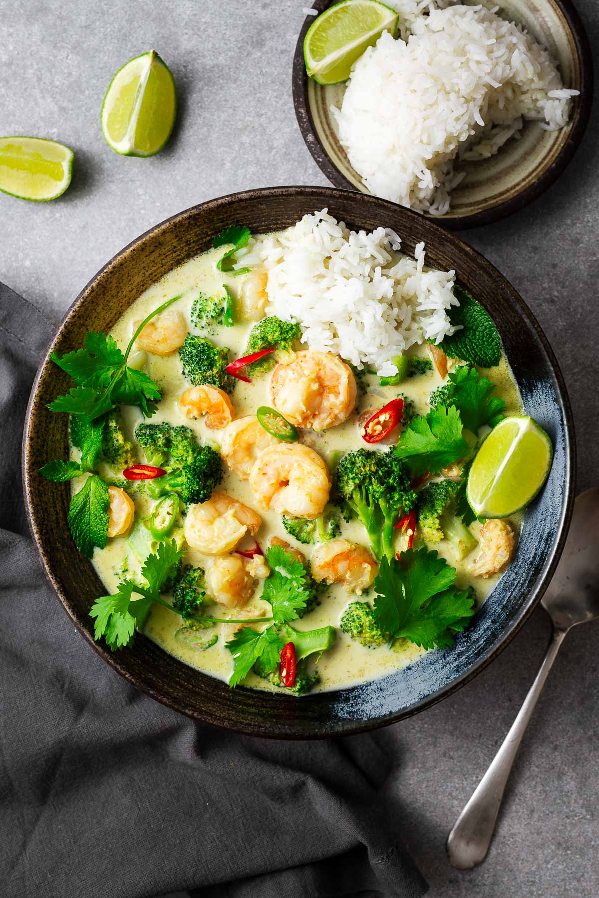 A five-ingredient Thai green curry with prawn tails and a side of rice, garnished with lime wedges and fresh herbs.
