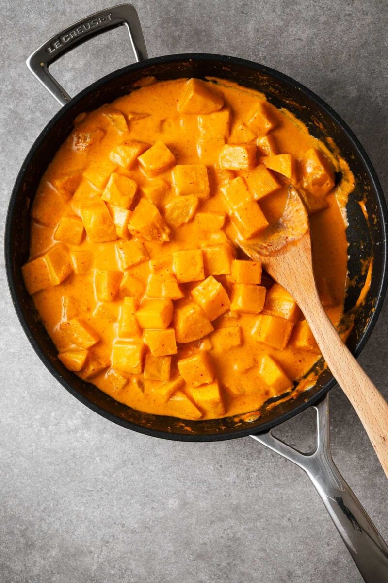 Cubed butternut being cooked in red curry sauce in a large frying pan.